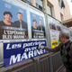 A far-right National Front supporter pastes an electoral poster reading “Patriots with Marine.”